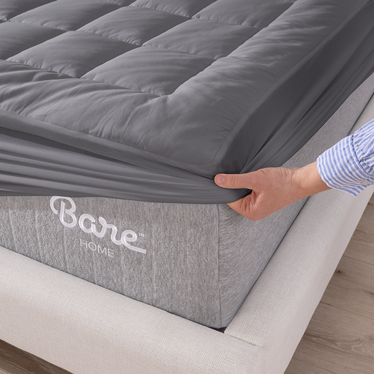 Hand fitting gray Cotton Top Mattress Pad onto a mattress corner