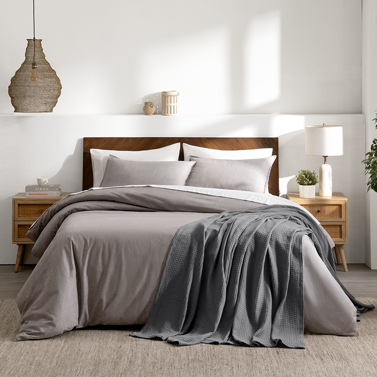 Bed with a gray waffle blanket next to a wood bench