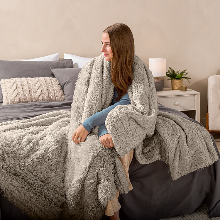 Woman sitting on a bed wrapped in a gray Shaggy Faux Fur Sherpa Blanket