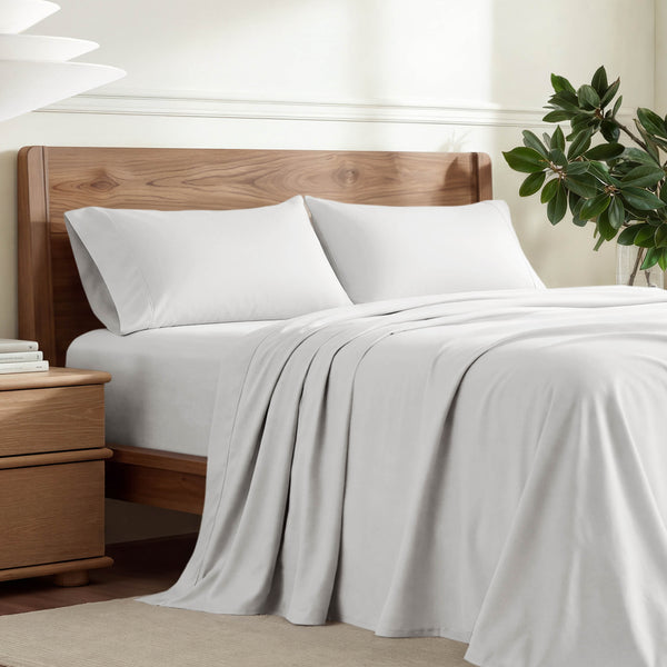 Percale sheets on a bed with a light wood headboard, styled in a warm, minimalist bedroom setting.