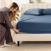 A woman is putting a fitted sateen sheet on a mattress