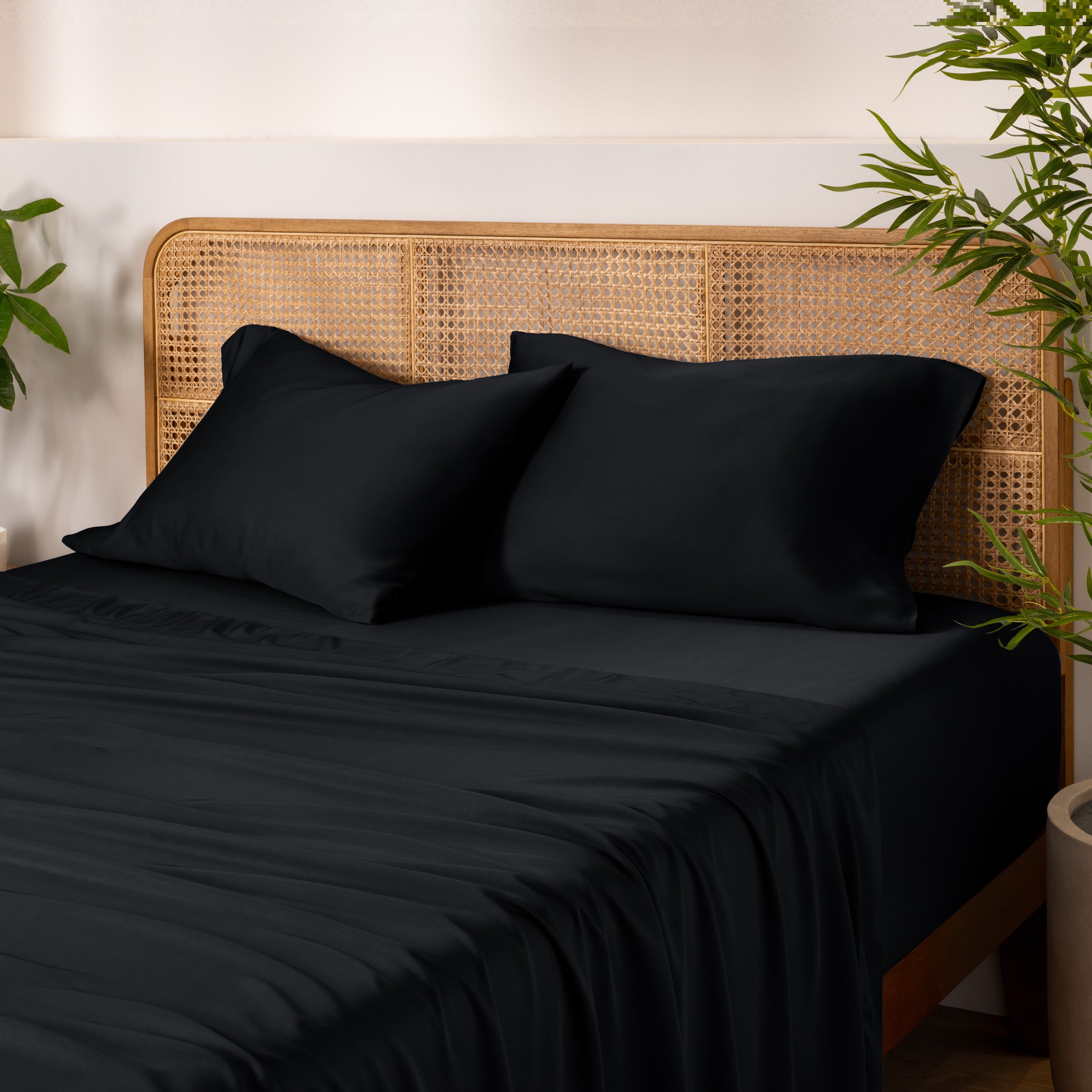 Bamboo bed sheets and pillows on a bed with a wicker headboard and plants in the background.