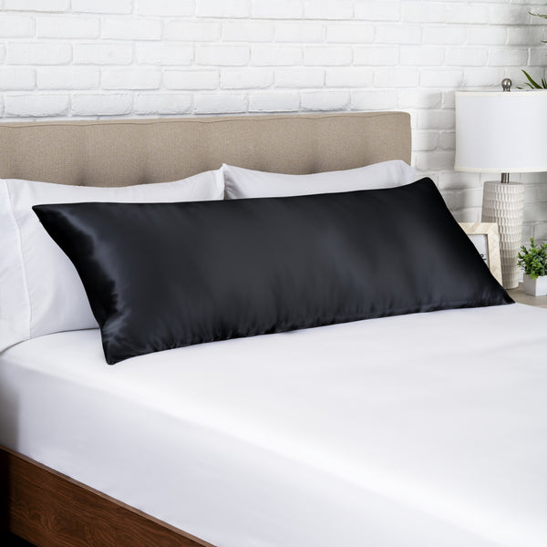 Black silk pillow on a bed with white bedding and a beige headboard.