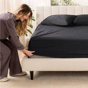 A woman is putting a fitted sateen sheet on a mattress