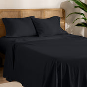 Organic cotton jersey bed sheets on a bed with a wicker headboard and plant in the background