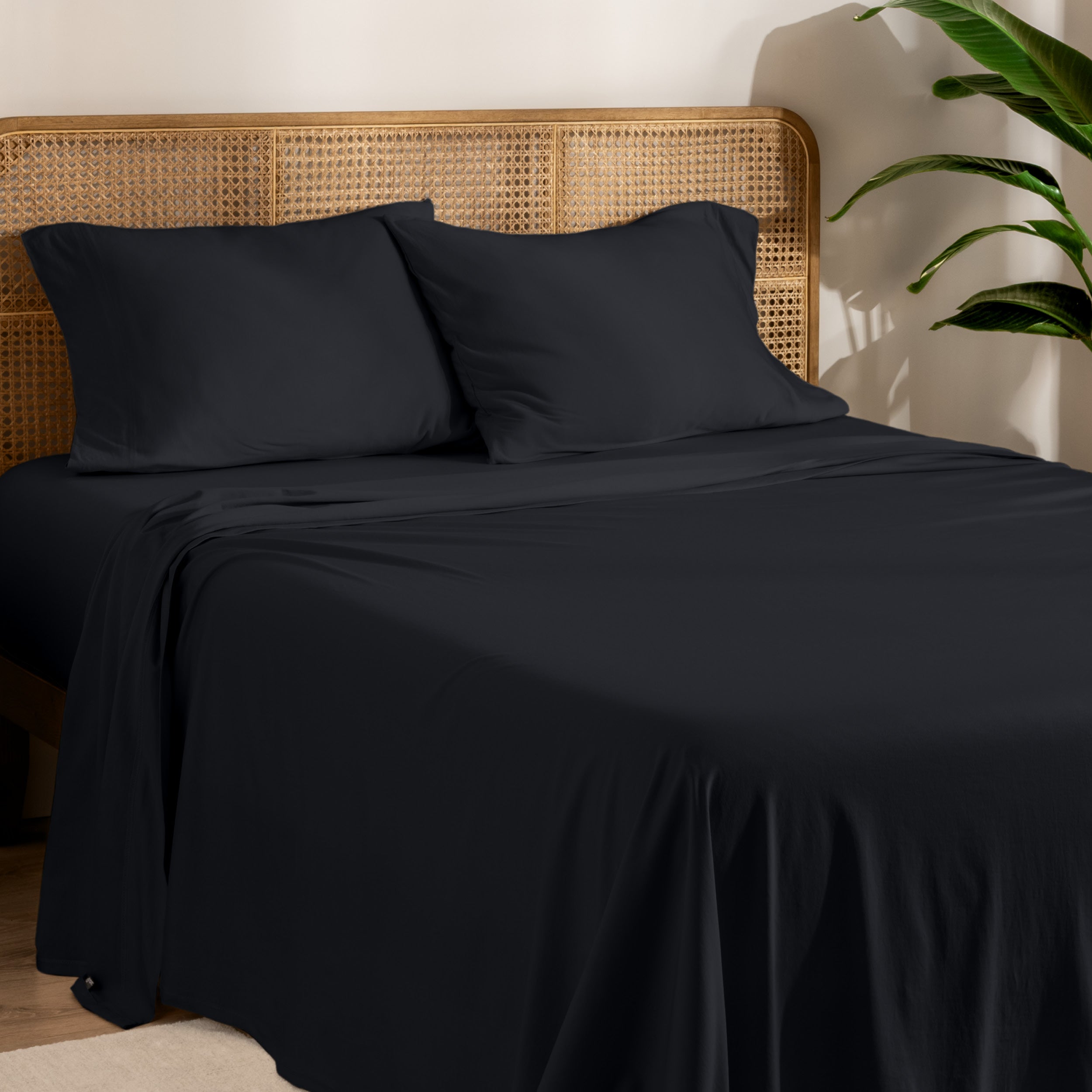 Organic cotton jersey bed sheets on a bed with a wicker headboard and plant in the background