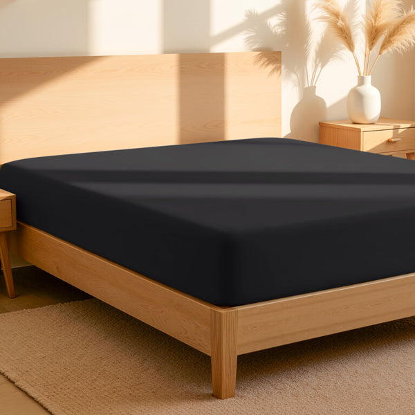 Fitted sheet on a bed in a bedroom setting with a lamp and plant.