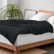 Weighted blanket on a bed with white pillows and a wooden headboard in a room with a plant and brick wall.