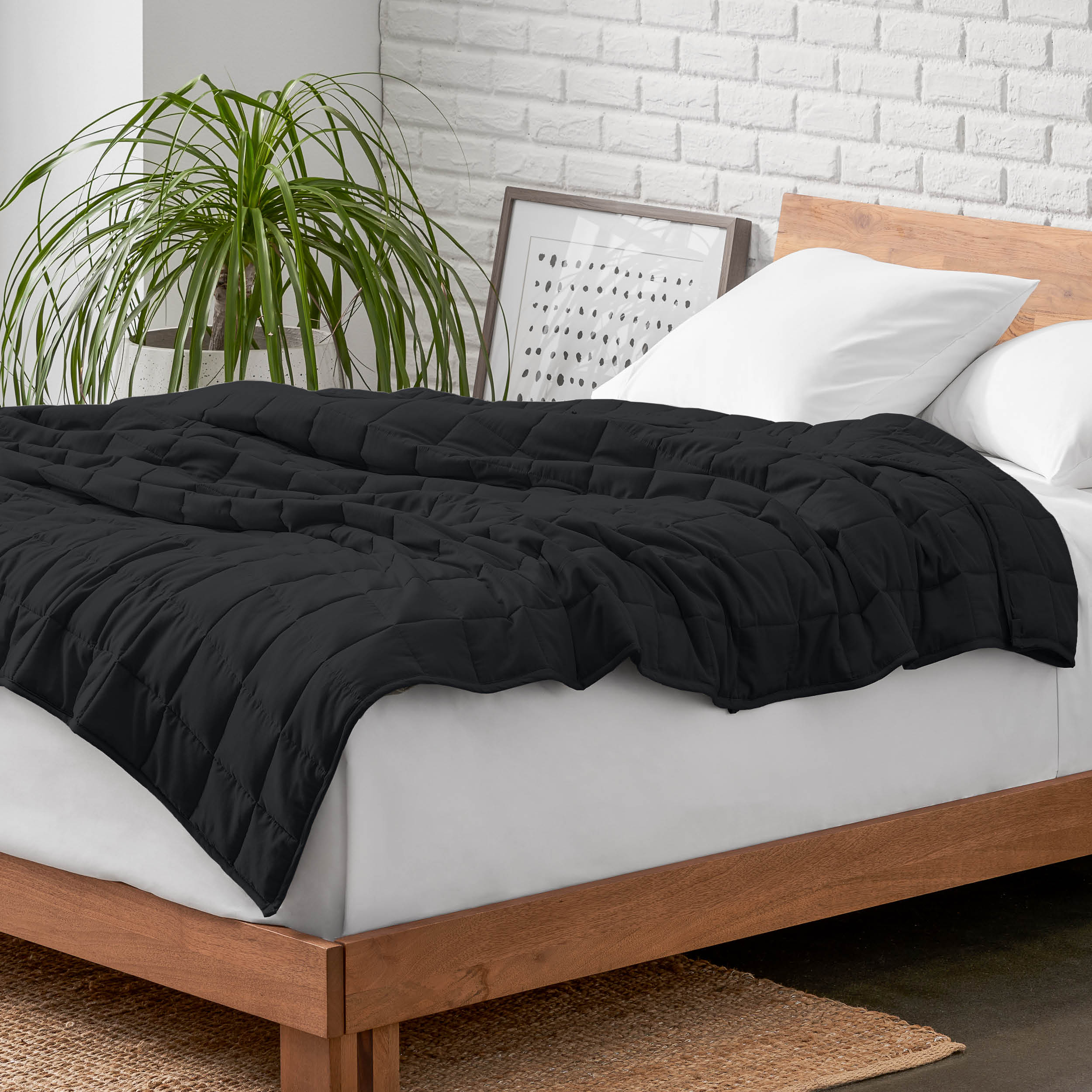 Weighted blanket on a bed with white pillows and a wooden headboard in a room with a plant and brick wall.