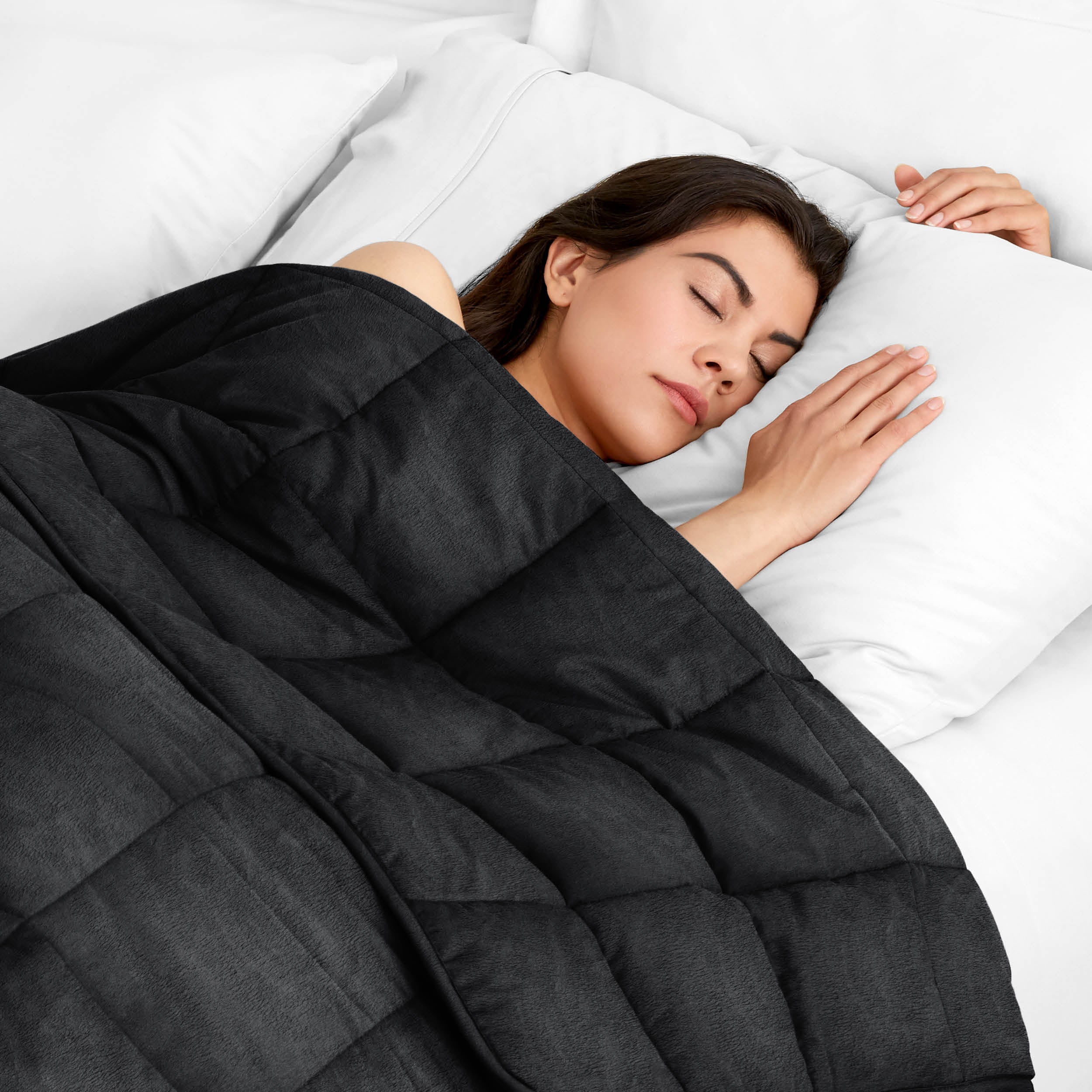 Woman sleeping peacefully under a weighted blanket with white pillows