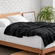 Weighted blanket on a bed with white pillows and a wooden headboard in a room with a plant and brick wall