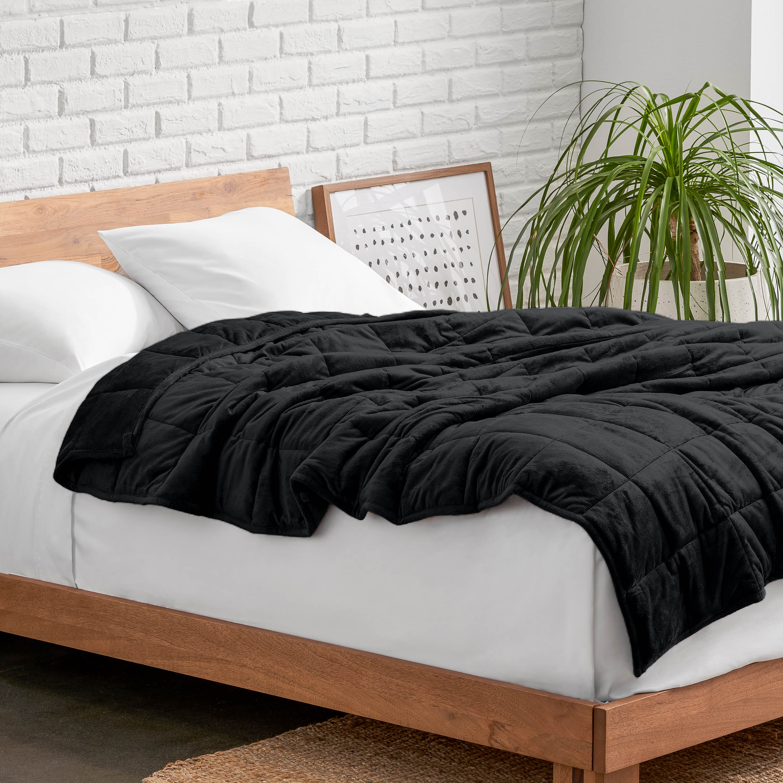 Weighted blanket on a bed with white pillows and a wooden headboard in a room with a plant and brick wall