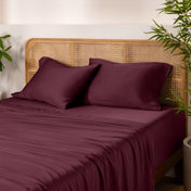 Bamboo bed sheets and pillows on a bed with a wicker headboard and plants in the background.