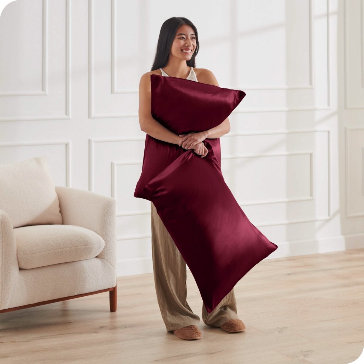 A woman standing while holding pillows with silk pillowcases on them