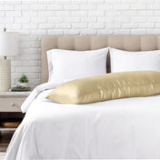 Body pillow on a bed with white bedding and a white brick wall background