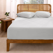 Bed with fitted sheet and pillows in a room with curtains and a plant.