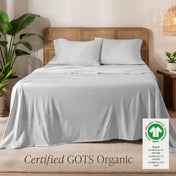 Jersey sheets on a bed with a wicker headboard in a room with plants and a lamp.