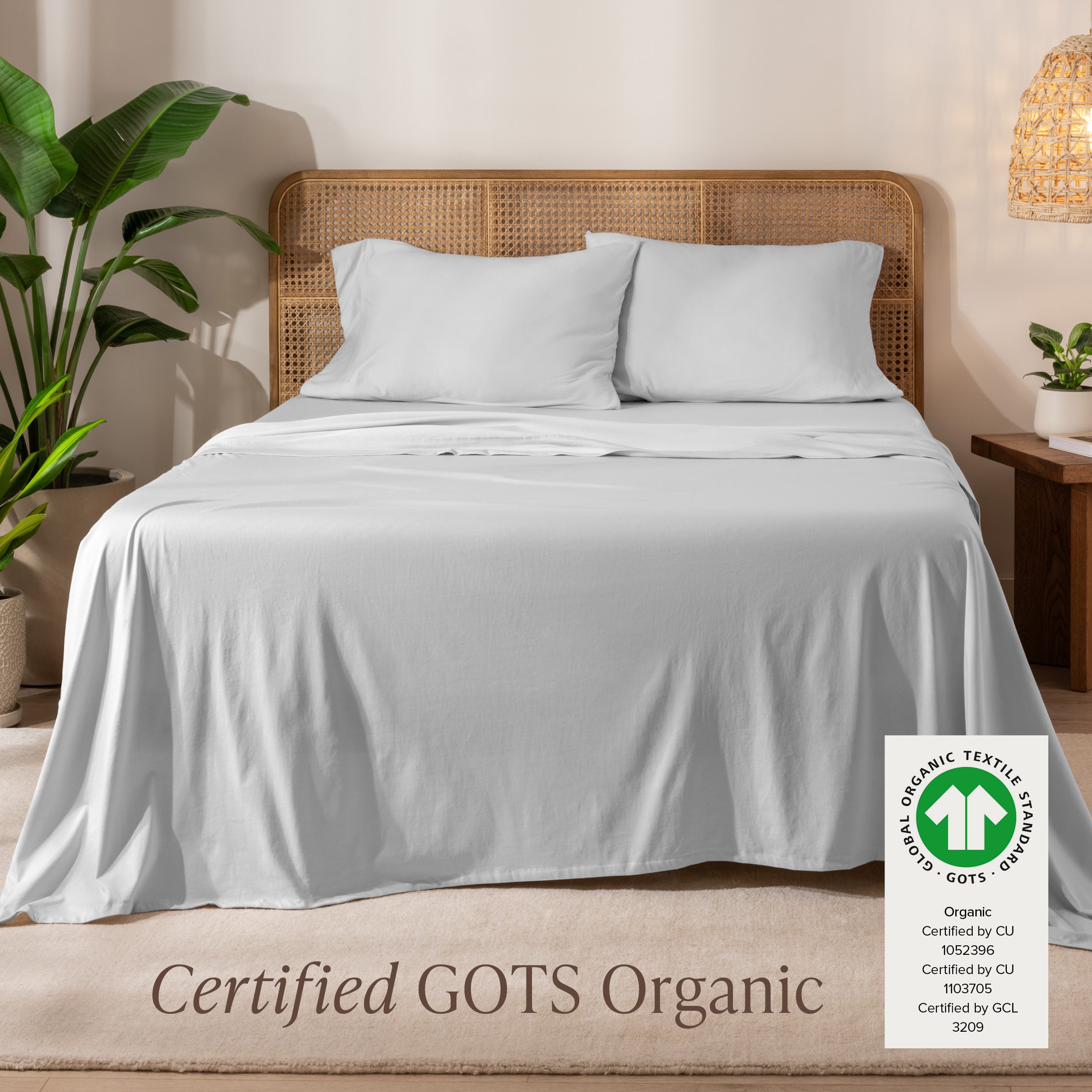 Jersey sheets on a bed with a wicker headboard in a room with plants and a lamp.