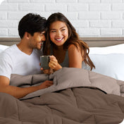 A couple sitting in bed with a reversible comforter over them