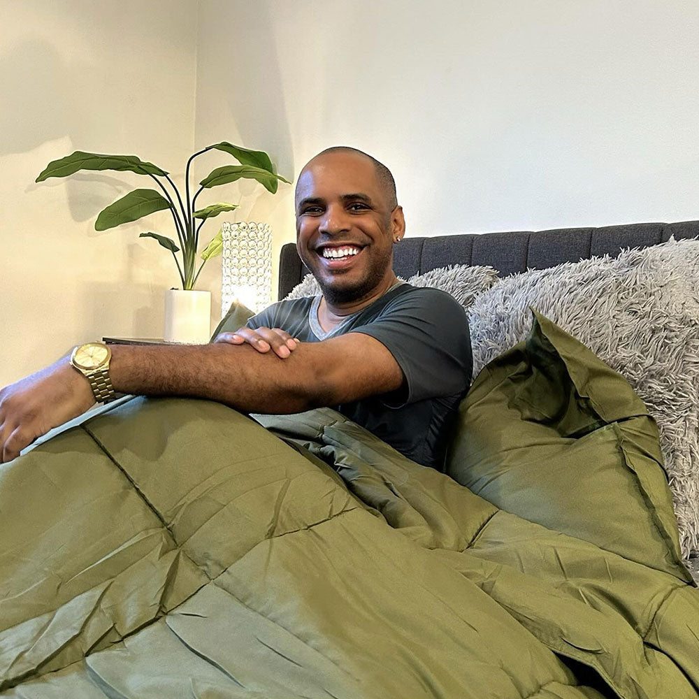 A older gentleman laying on his bed under a forest green comforter