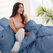 Woman sitting on a bed under duvet cover with a plant in the background