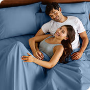 A couple is relaxing in bed with pillows behind them
