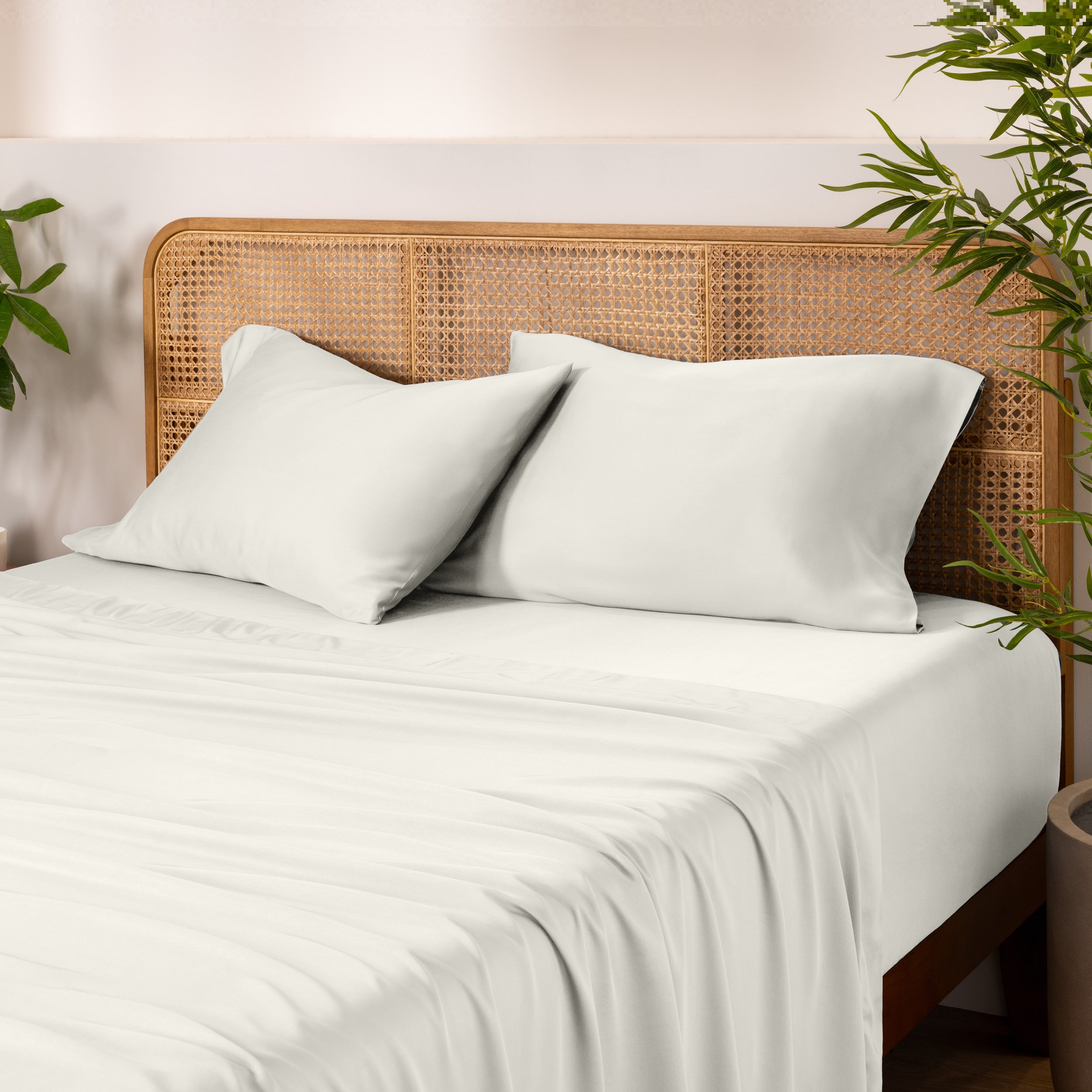 Bamboo bed sheets and pillows on a bed with a wicker headboard and plants in the background.
