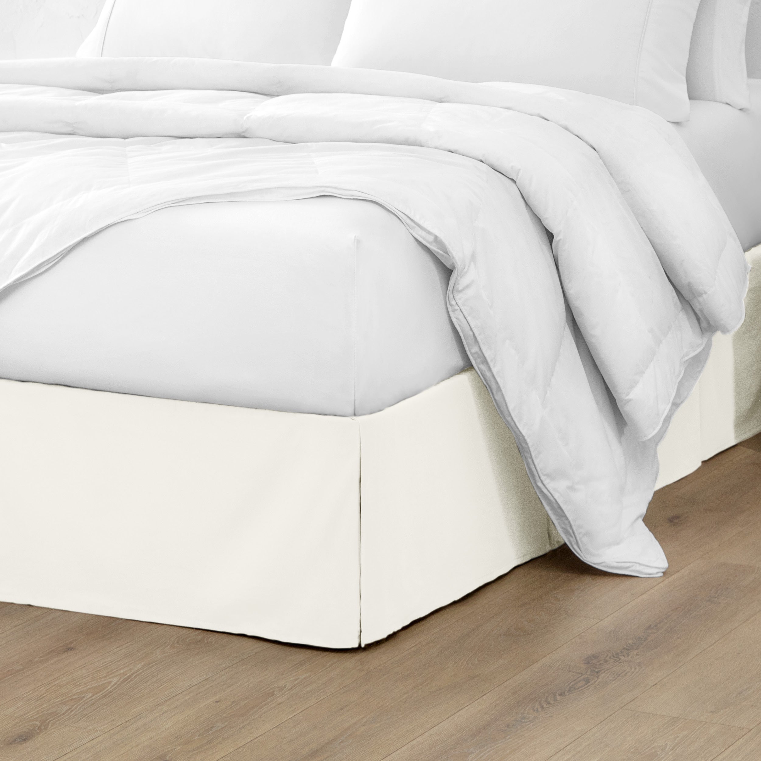 A modern bed with a microfiber bed skirt with pleats on the corners and midway on each side