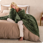 A woman sitting on the end of a bed with a shaggy blanket wrapped around her