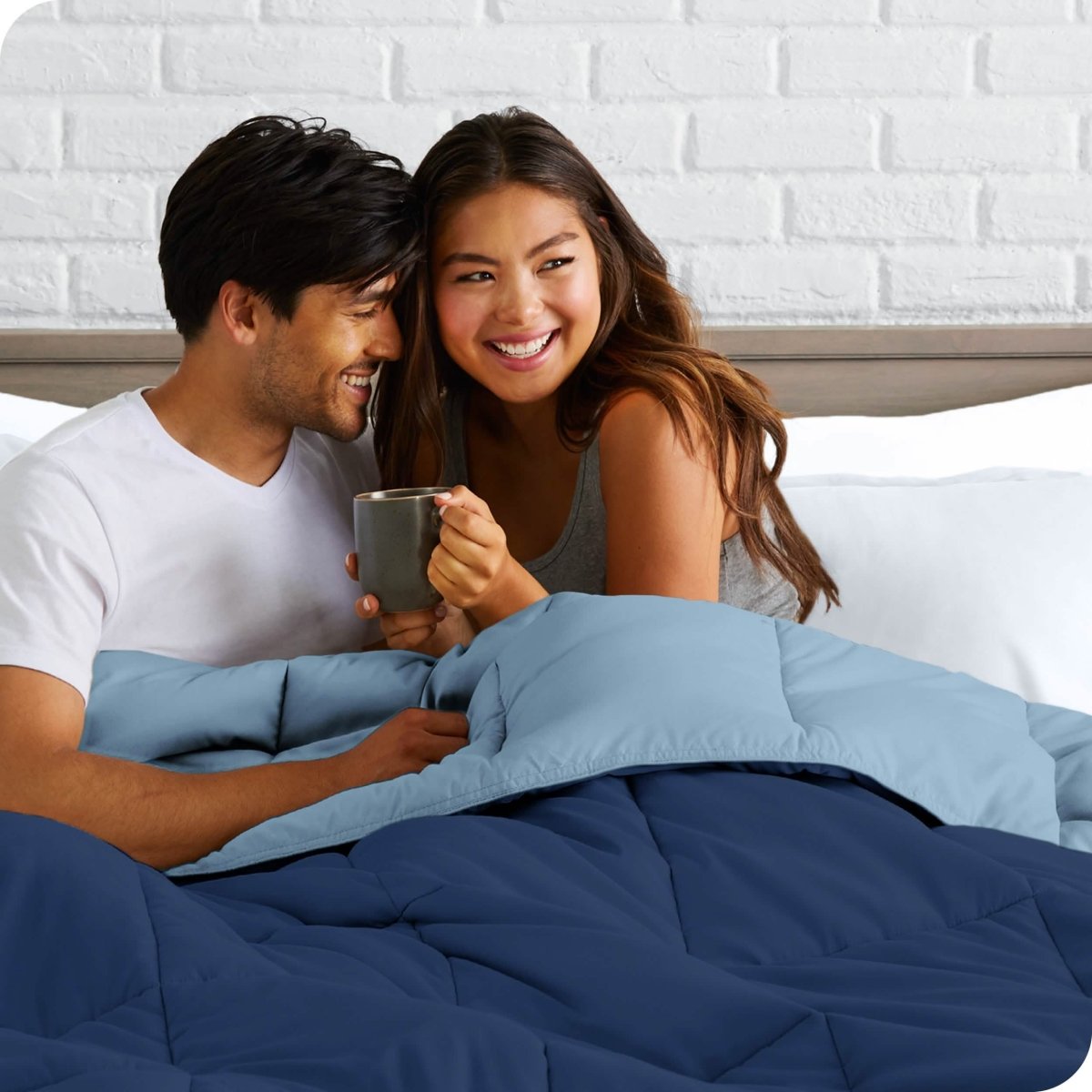 A couple sitting in bed with a reversible comforter over them