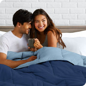 A couple sitting in bed with a reversible comforter over them