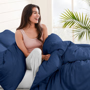 Woman sitting on a bed under duvet cover with a plant in the background