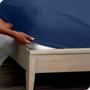 A man is kneeling while putting a fitted sheet on a mattress