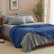 A bed made with grey sheets and a microplush blanket