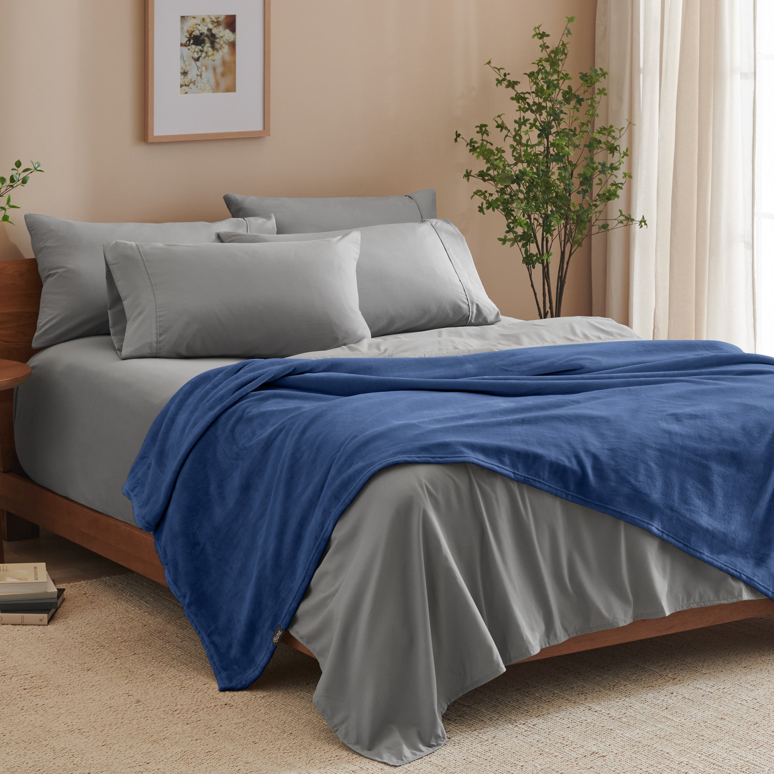 A bed made with grey sheets and a microplush blanket