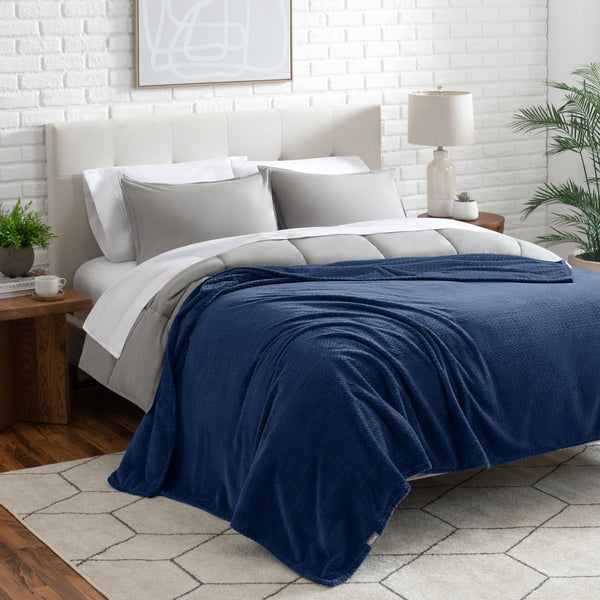 Neatly made bed with a blanket draped over the end of the bed