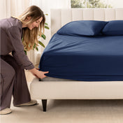 A woman is putting a fitted sateen sheet on a mattress