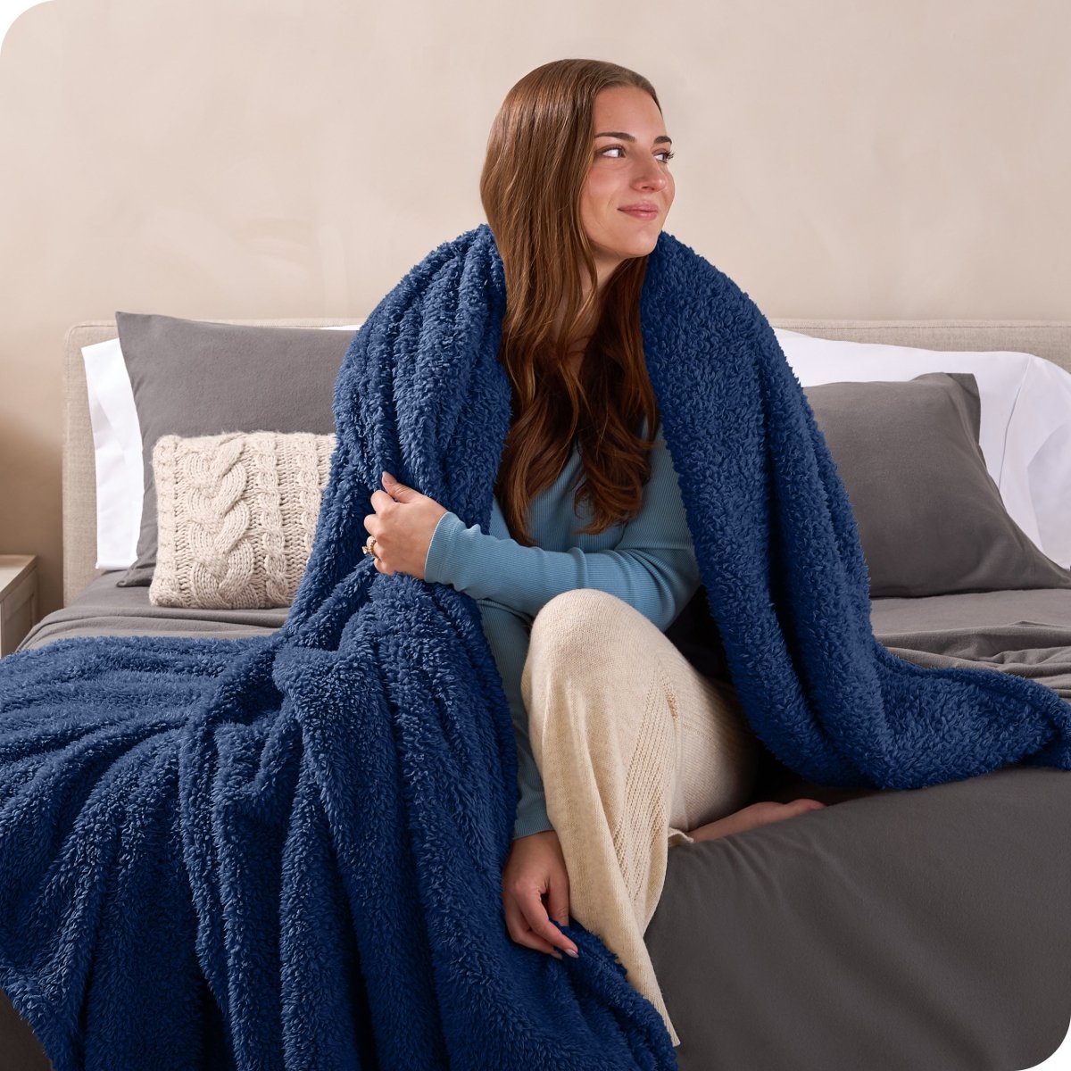 A woman sitting on a bed wrapped in a sherpa blanket