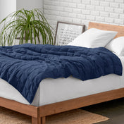 Weighted blanket on a bed with white pillows and a wooden headboard in a room with a plant and brick wall.