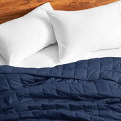 Cotton weighted blanket on a bed with white pillows against a wooden headboard.