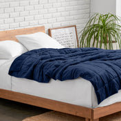 Weighted blanket on a bed with white pillows and a wooden headboard in a room with a plant and brick wall