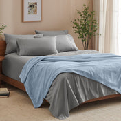 A bed made with grey sheets and a microplush blanket