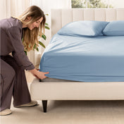 A woman is putting a fitted sateen sheet on a mattress