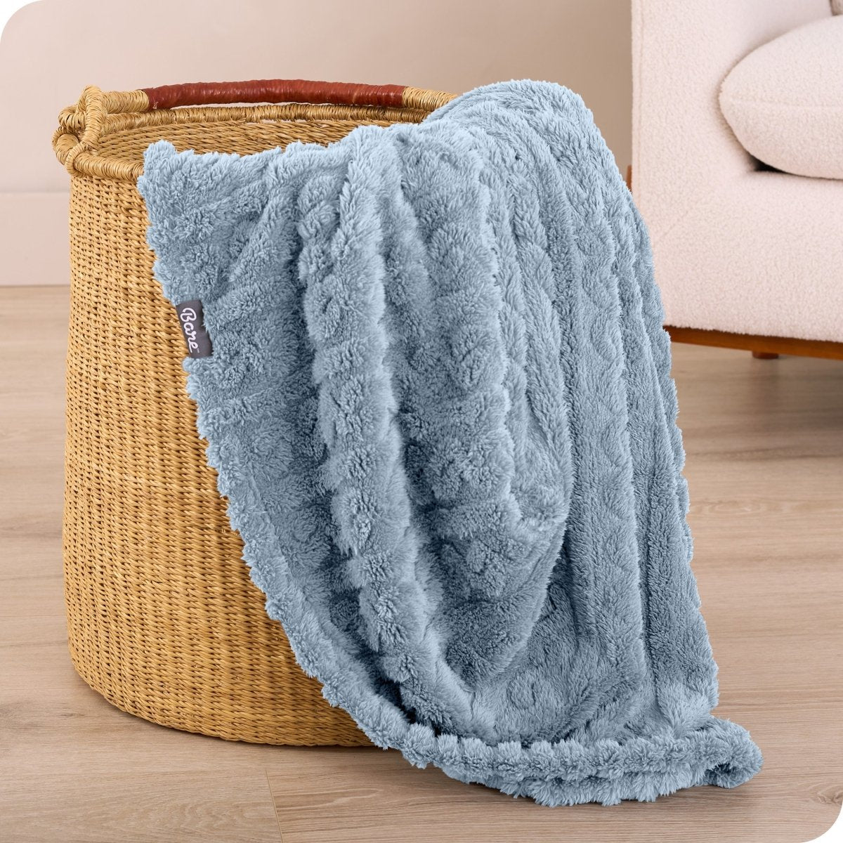 A sherpa blanket is hanging over the edge of a woven hamper