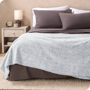 A textured sherpa blanket draped over the end and side of a bed