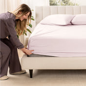 A woman is putting a fitted sateen sheet on a mattress
