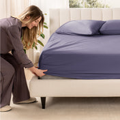 A woman is putting a fitted sateen sheet on a mattress