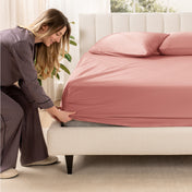 A woman is putting a fitted sateen sheet on a mattress
