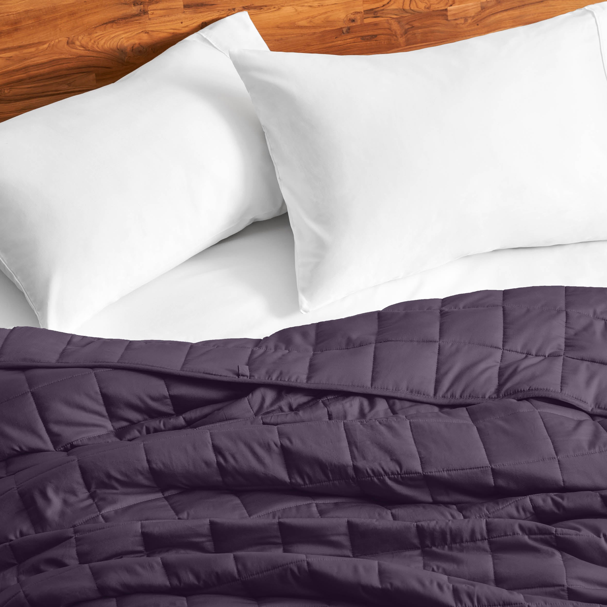 Cotton weighted blanket on a bed with white pillows against a wooden headboard.