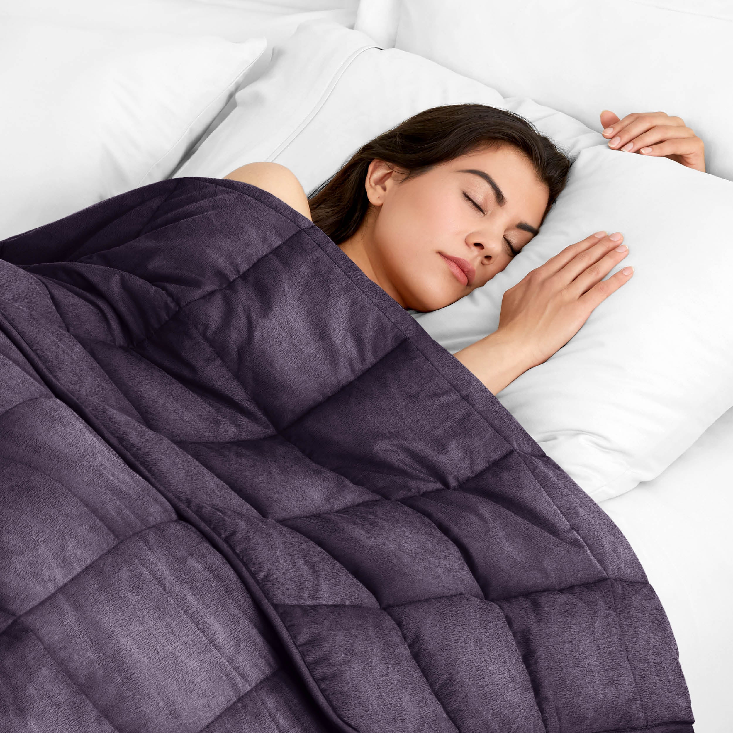 Woman sleeping peacefully under a weighted blanket with white pillows